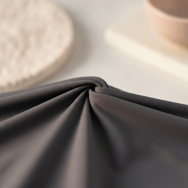 Close-up of charcoal activewear fabric, gently stretched to show its resilience and snap-back recovery after washing.
